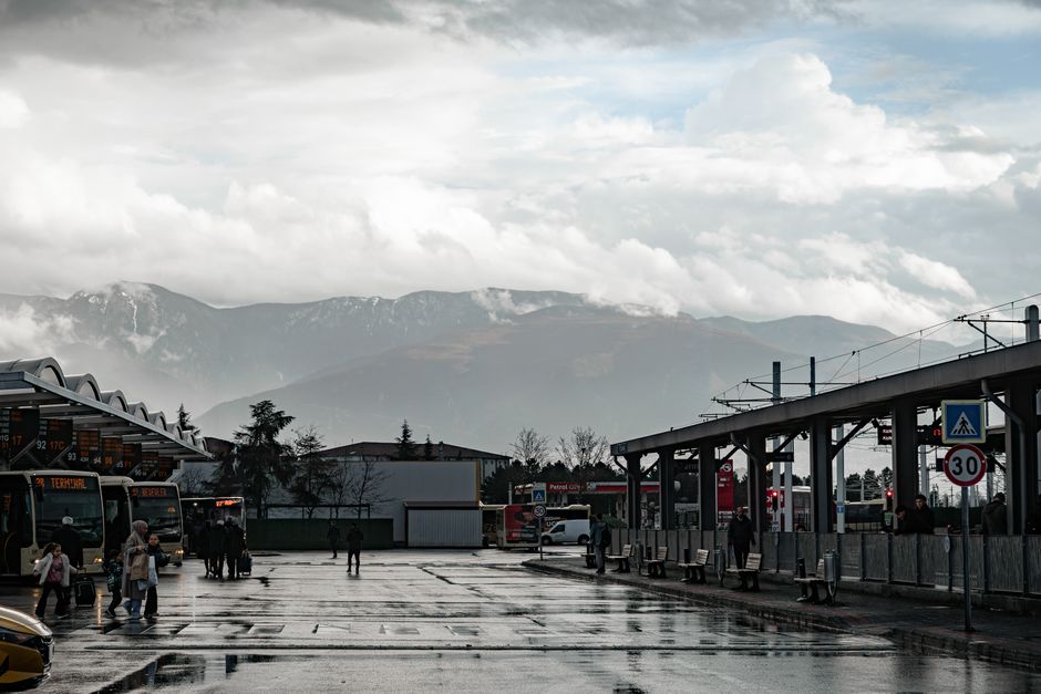 Bus terminal scene with passengers and distant mountains, capturing urban commute life.